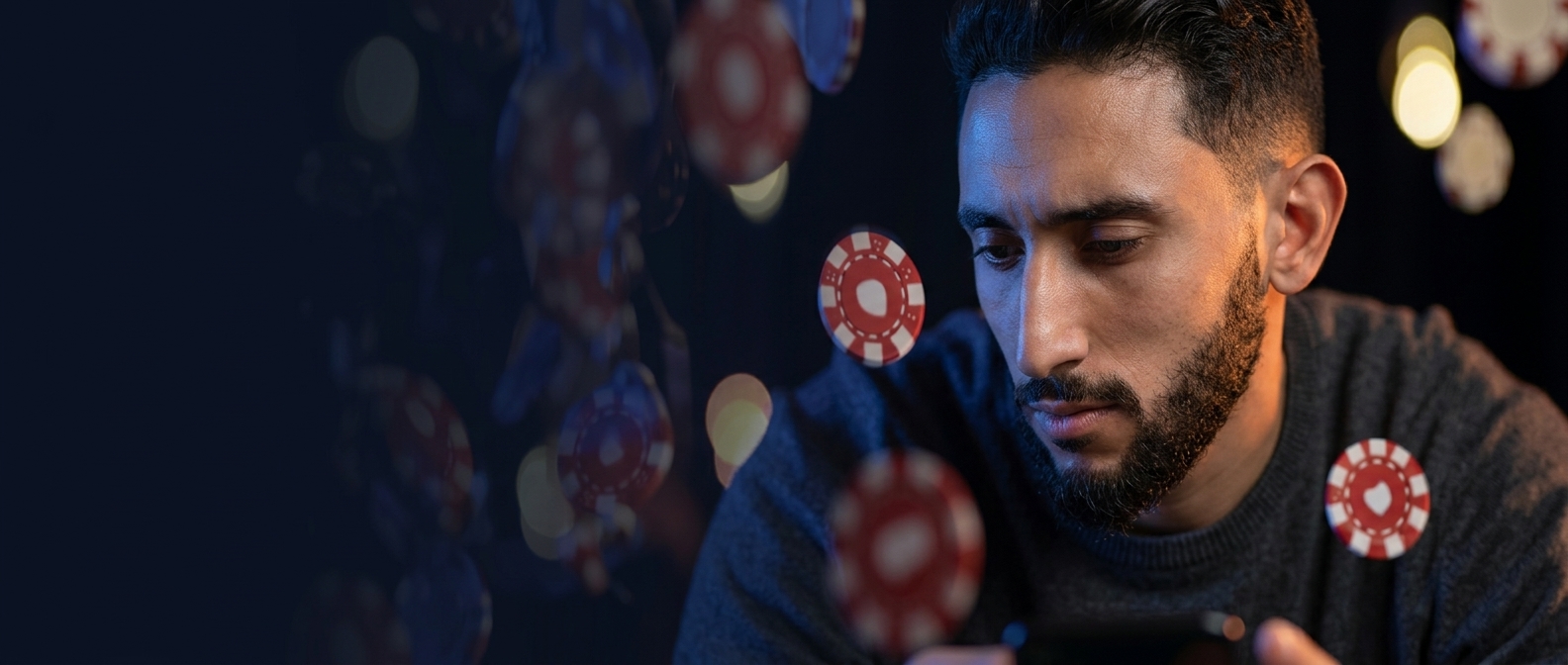 Joueur marocain concentré sur son téléphone, jetons de casino flottants — ambiance nocturne bleue et ambrée